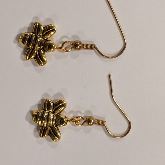 A pair of gold-toned bee dangle earrings with nickel free alloy french hook ear wires placed on a white surface.