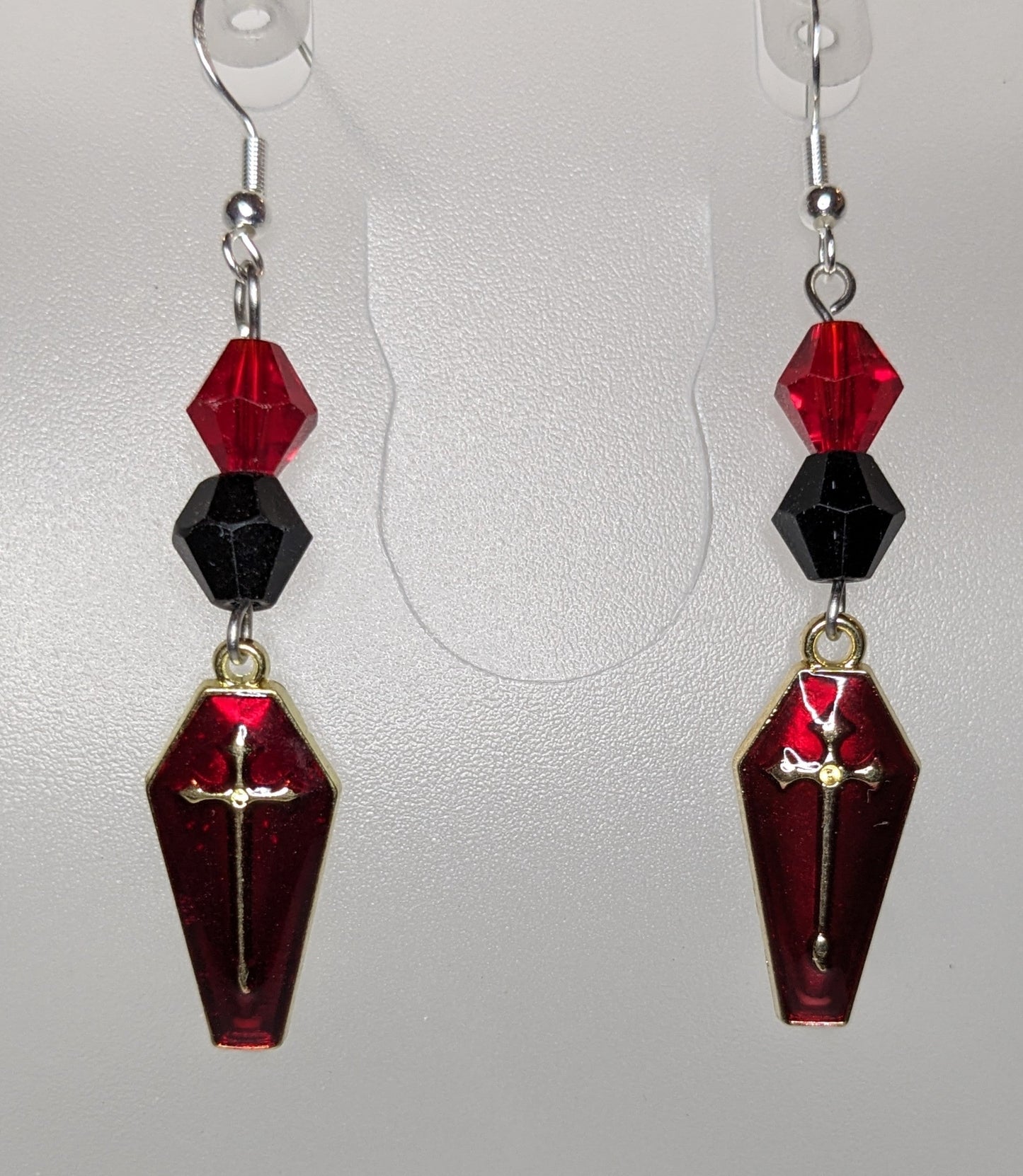 A pair of Vamp Goth Earrings featuring coffin-shaped charms in enameled red with a gold cross with faceted black and red bead accents.