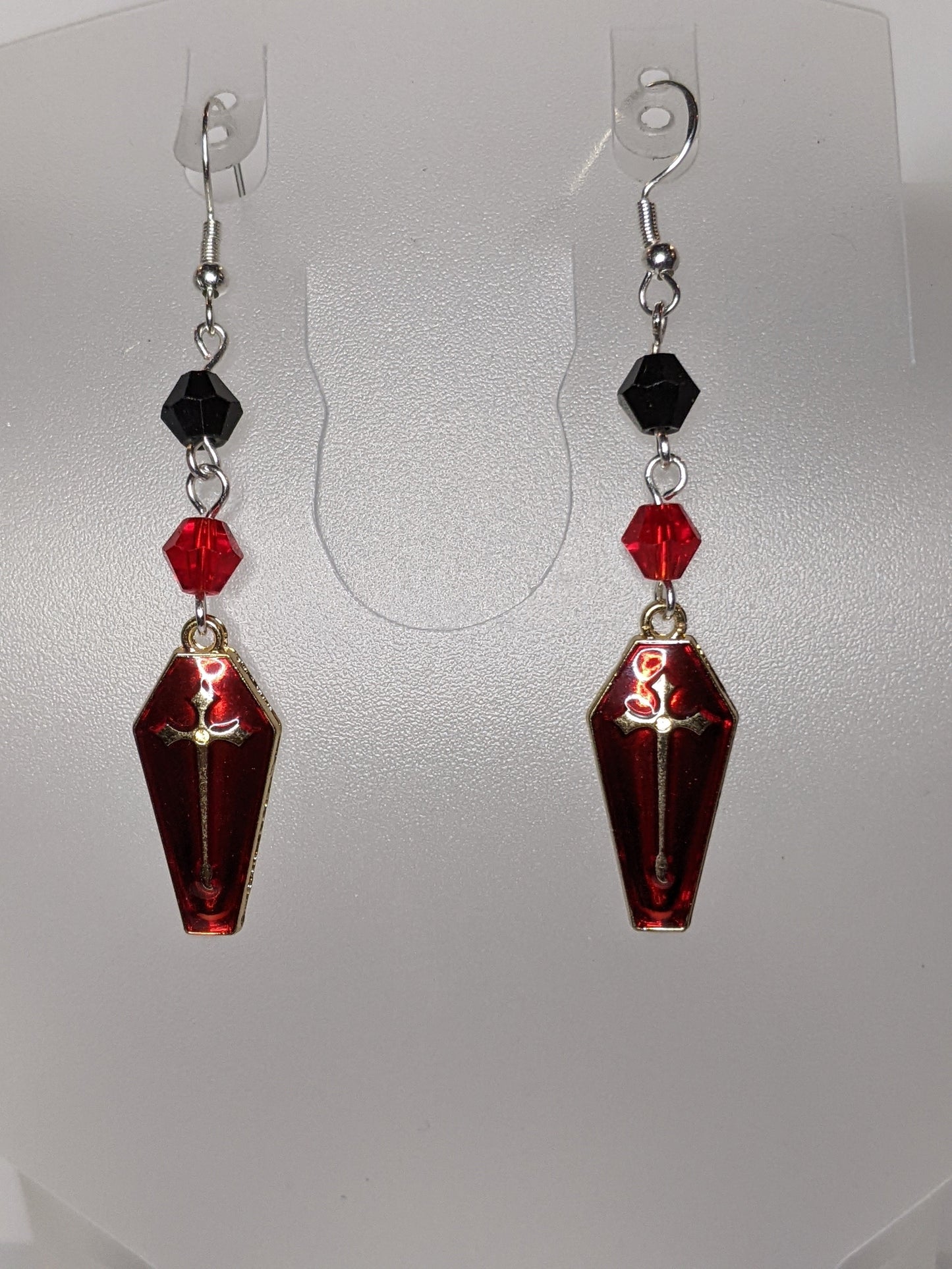 A pair of Vamp Goth Earrings featuring coffin-shaped charms enameled in red with a gold cross with faceted black and red bead accents.