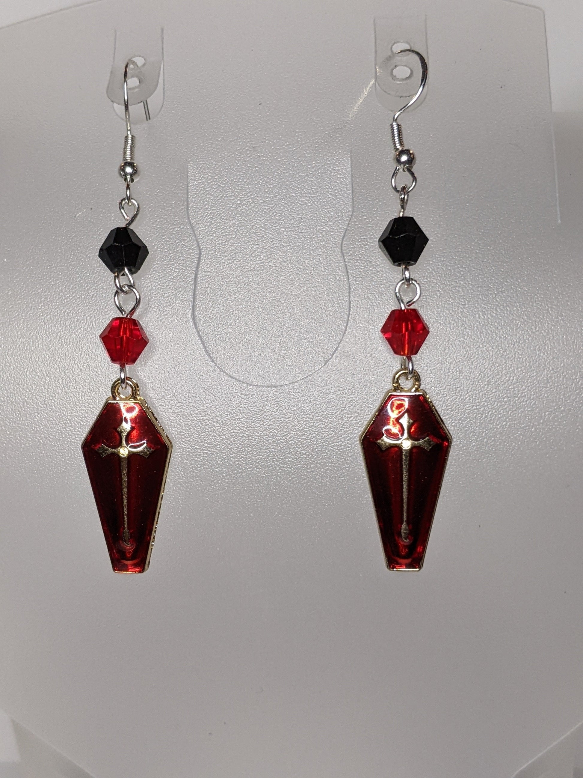 A pair of Vamp Goth Earrings featuring coffin-shaped charms enameled in red with a gold cross with faceted black and red bead accents.